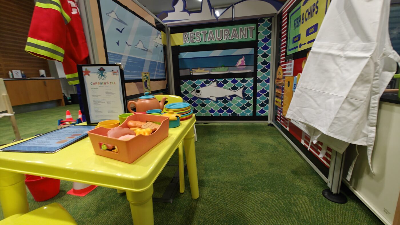Modular restaurant play zone panel fully dressed with custom wooden steering wheel, navigation props, and tactile toys.